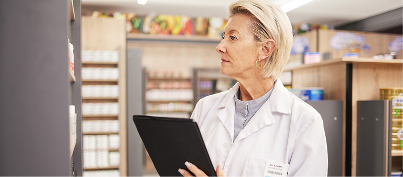 A person wearing a pharmaceutical jacket, holding a clipboard.