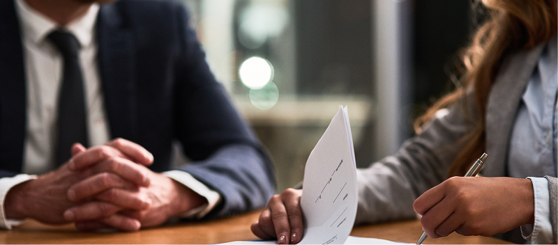 The hands of two business people sifting through papers at a desk.