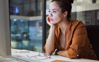 A woman sitting at a desk looking at a screen in deep in thought.