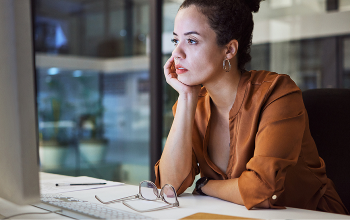 A woman sitting at a desk looking at a screen in deep in thought.