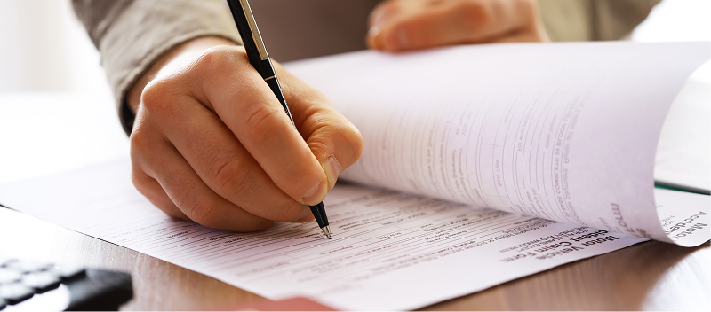 A close up of a hand signing papers.